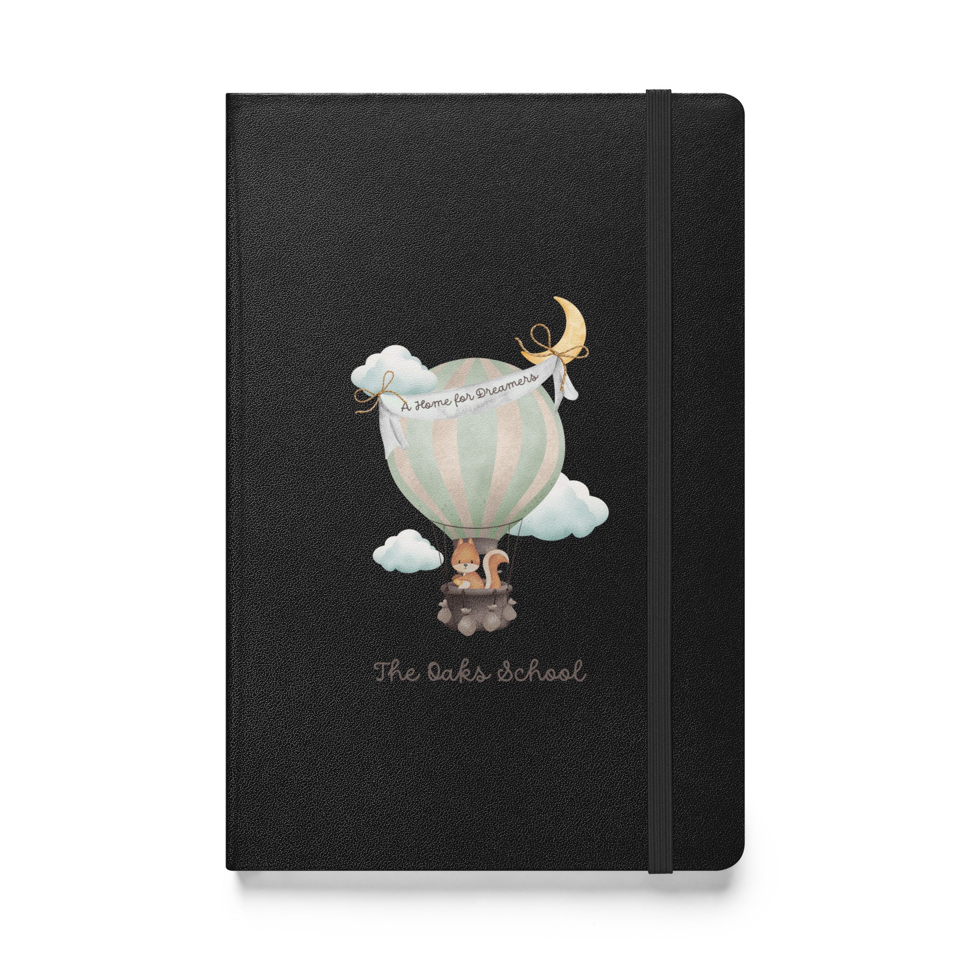 Product mockup: A black colored journal on a white background featuring a hot air balloon containing a squirrel and text that says "The Oaks School" and "A Home for Dreamers."