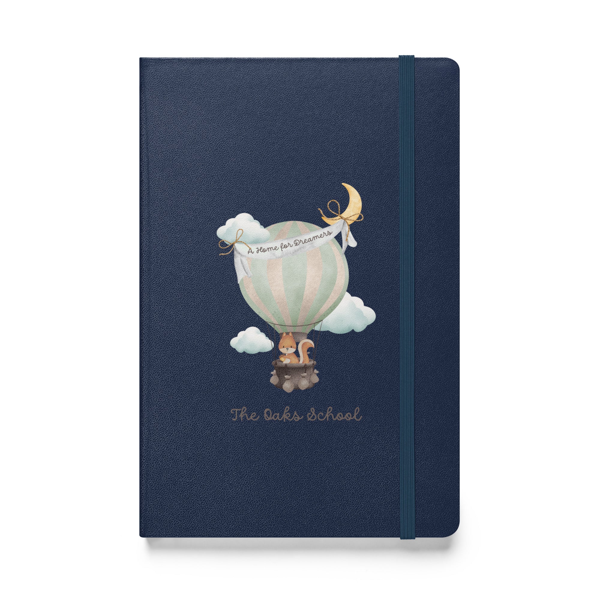 Product mockup: A navy colored journal on a white background featuring a hot air balloon containing a squirrel and text that says "The Oaks School" and "A Home for Dreamers."