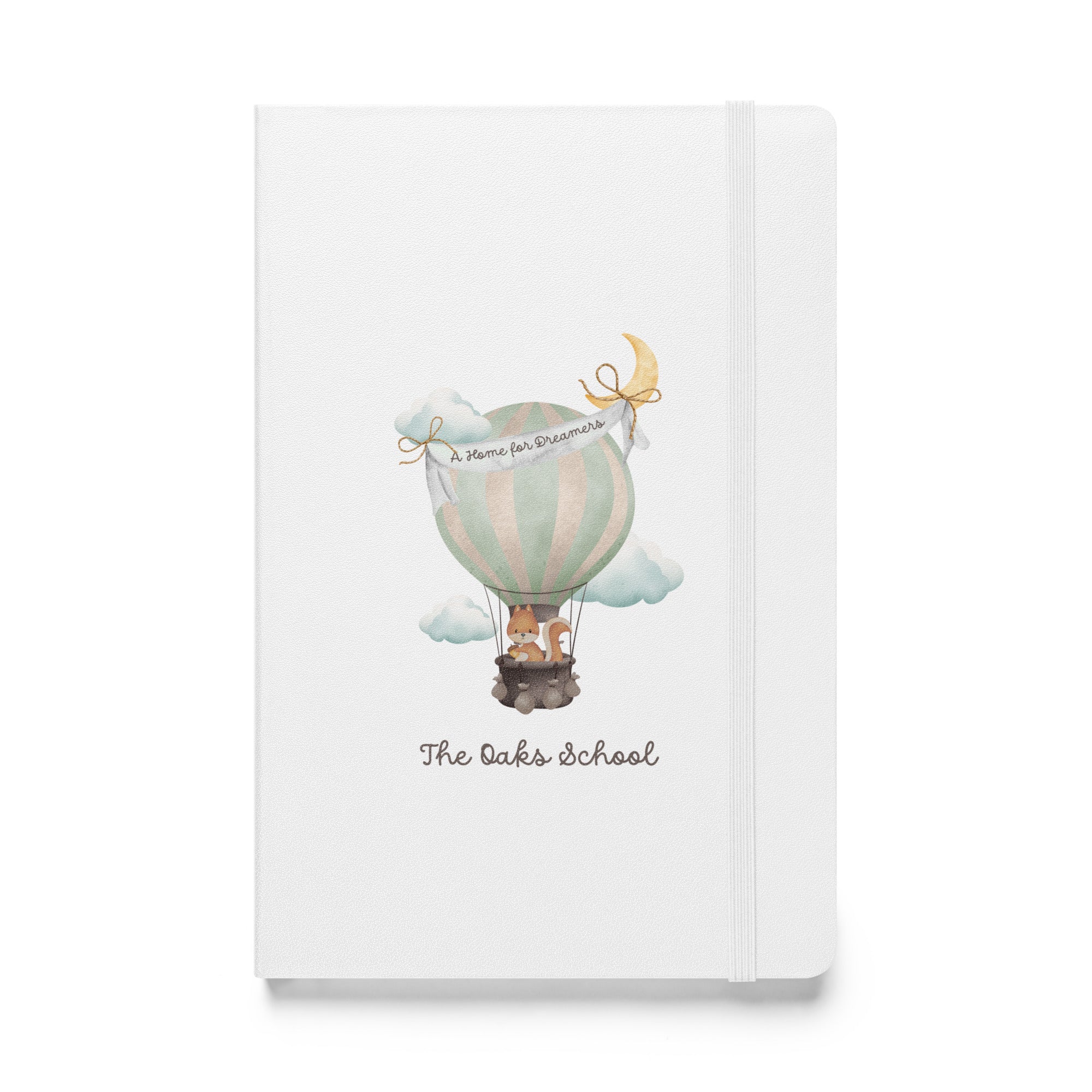 Product mockup: A white colored journal on a white background featuring a hot air balloon containing a squirrel and text that says "The Oaks School" and "A Home for Dreamers."