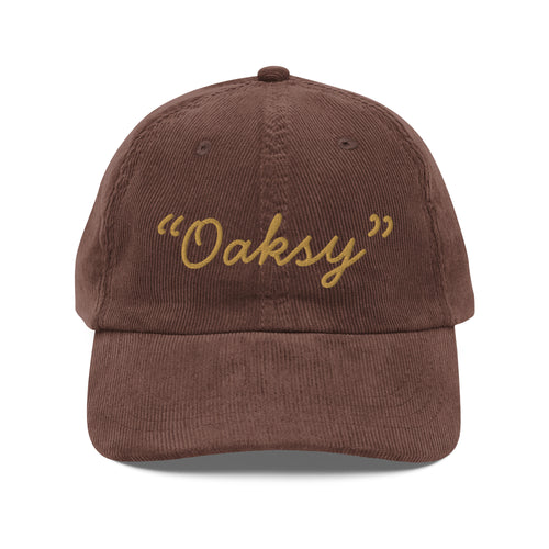 Product mockup:  A brown corduroy cap on a white background featuring gold lettering in a handwriting font that says "Oaksy" in quotes