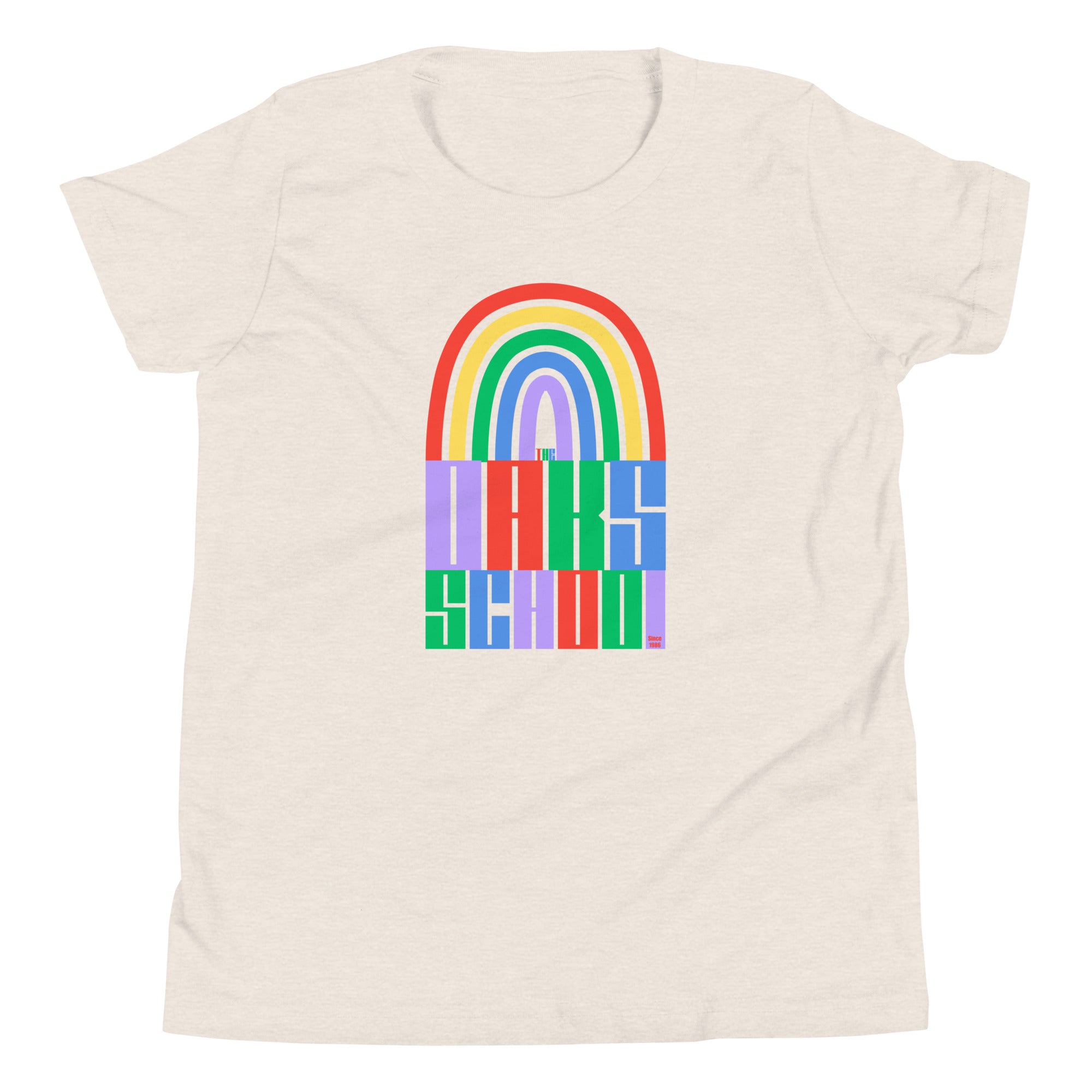 Product mockup: A heather dust colored tshirt on a white background featuring a rainbow illustration flowing into rainbow colored block letters that say "The Oaks School"