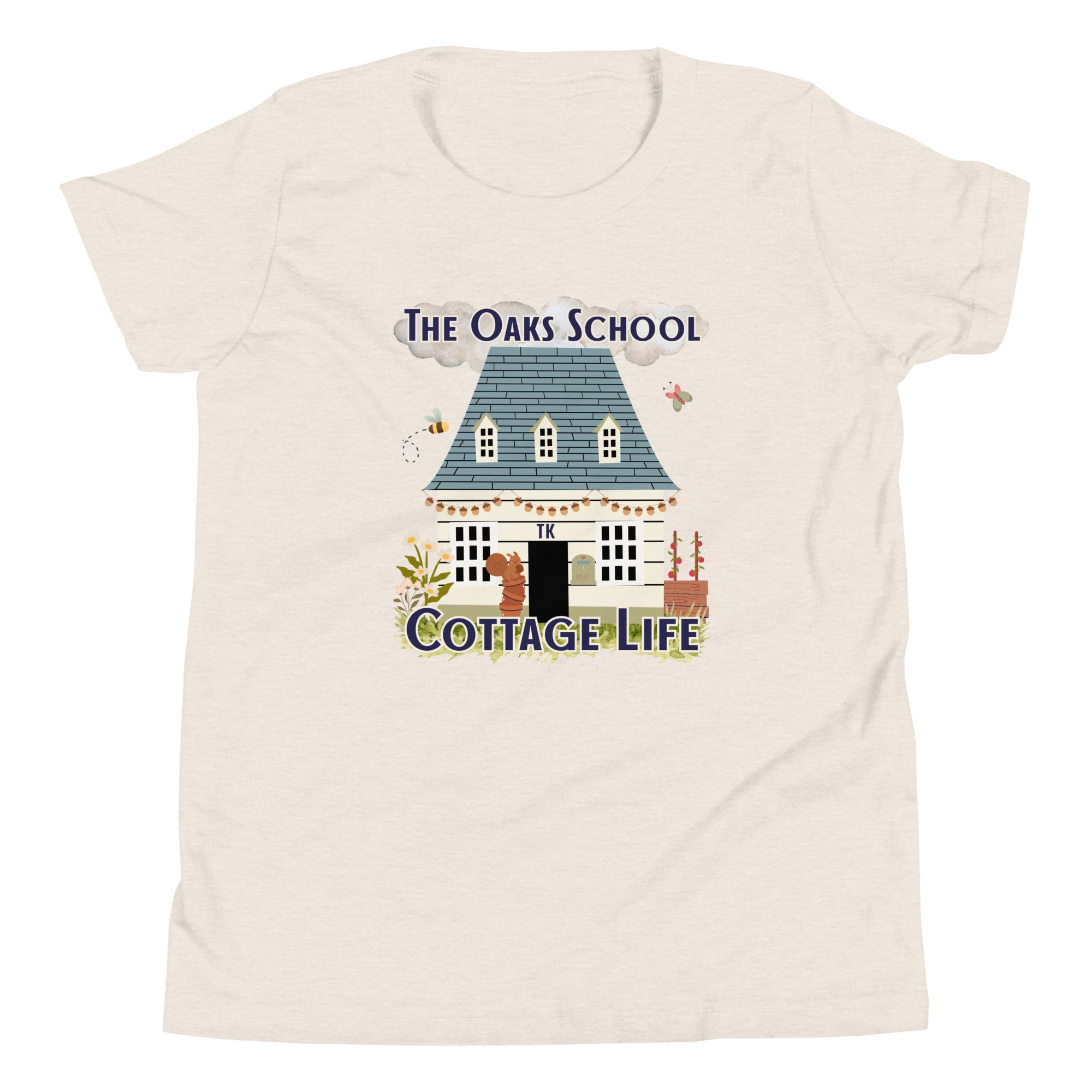 Product mockup: A heather dust colored tshirt on a white background featuring an illustration of a white cottage and the text "The Oaks School" and "Cottage Life"