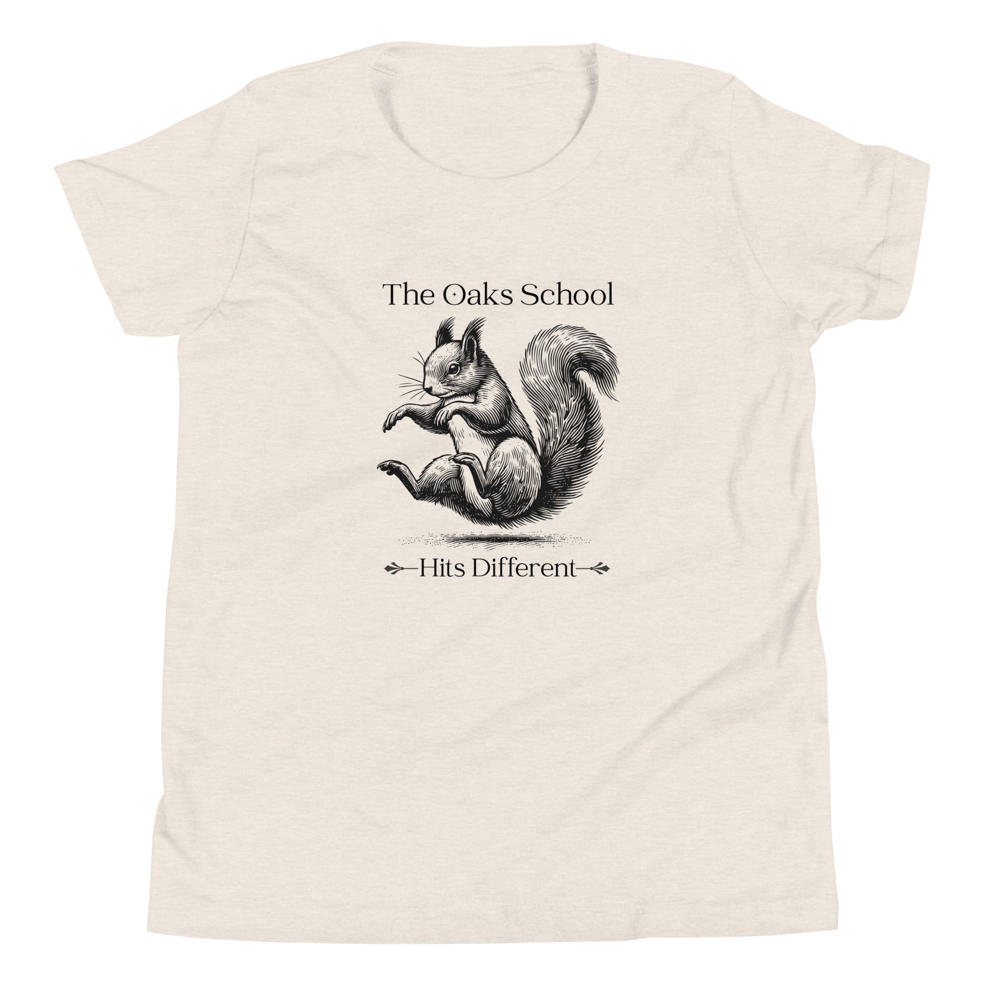 Product mockup: A heather dust colored tshirt on a white background featuring an illustration of a squirrel landing on its bottom and the text "The Oaks School" and "Hits Different"