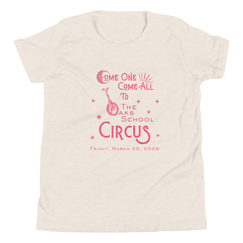 Product mockup: Heather dust colored tee with pink, weathered text "Come one, Call All to The Oaks School Circus, Friday, March 20, 2026." The "O" in "Oaks" is a unicycle wheel, the "C" in the first "Come" is a crescent moon, and there are stars sprinkled throughout.